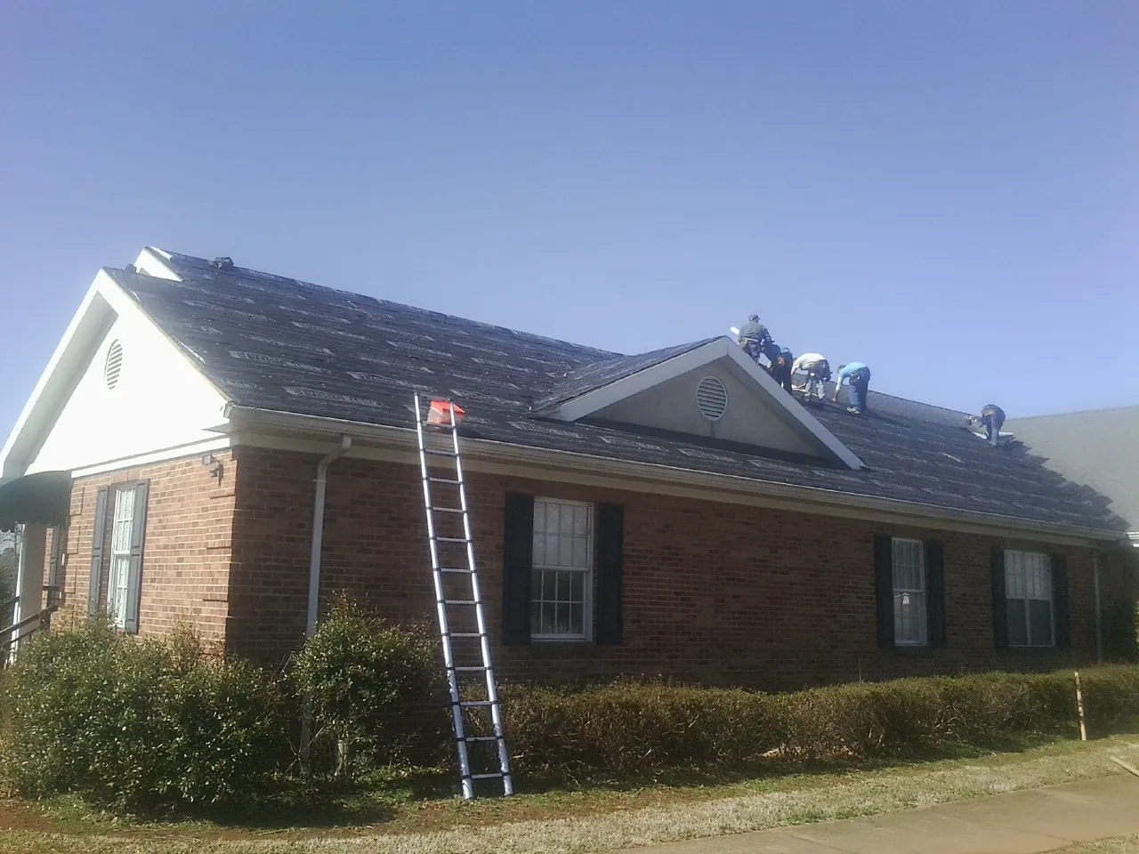 Crew tearing shingles off a brick ranch roof with a ladder set — Metal Roof Repair work by our crew in Noblesville