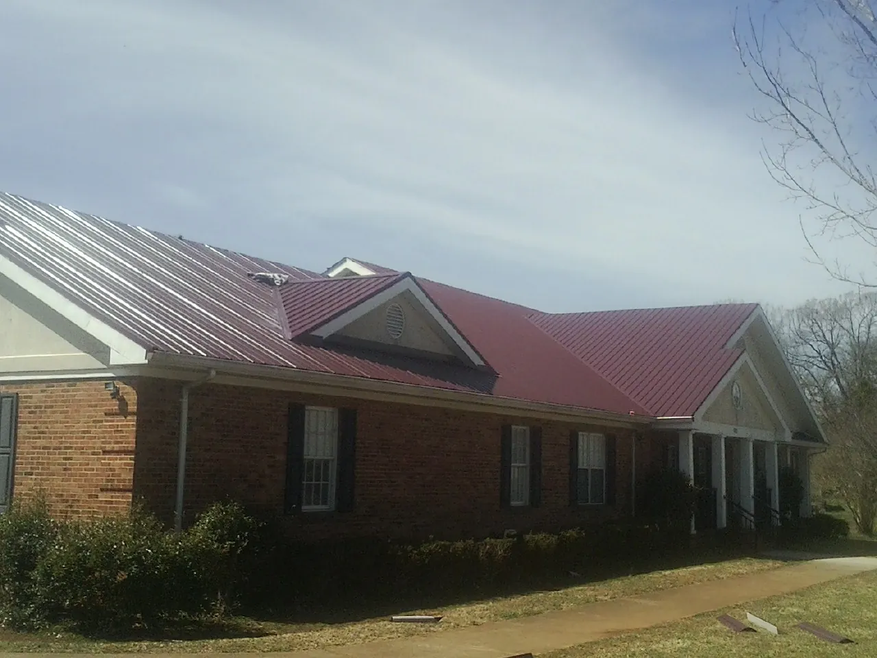 Red metal roof with gabled entries on a long brick building, from a Hail Damage Roof Repair job in Noblesville