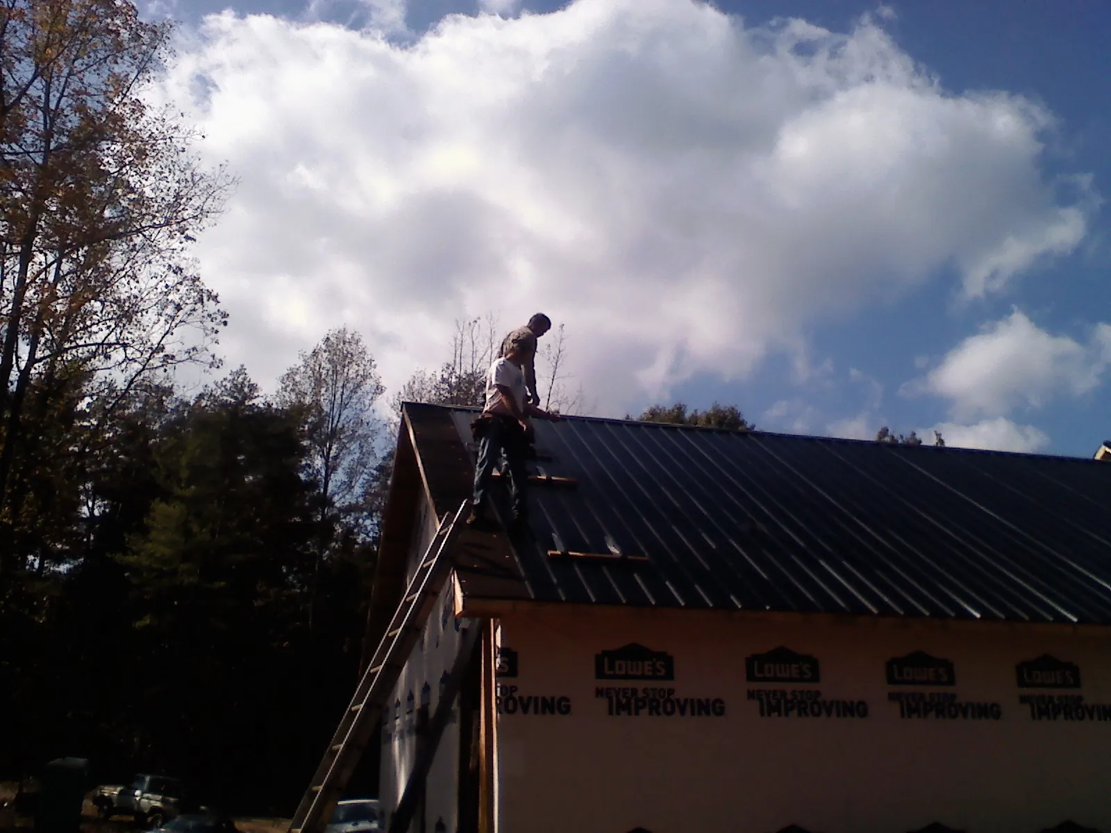Roofer fastening dark metal panels high against a cloudy sky, from a Roof Inspection job in Noblesville