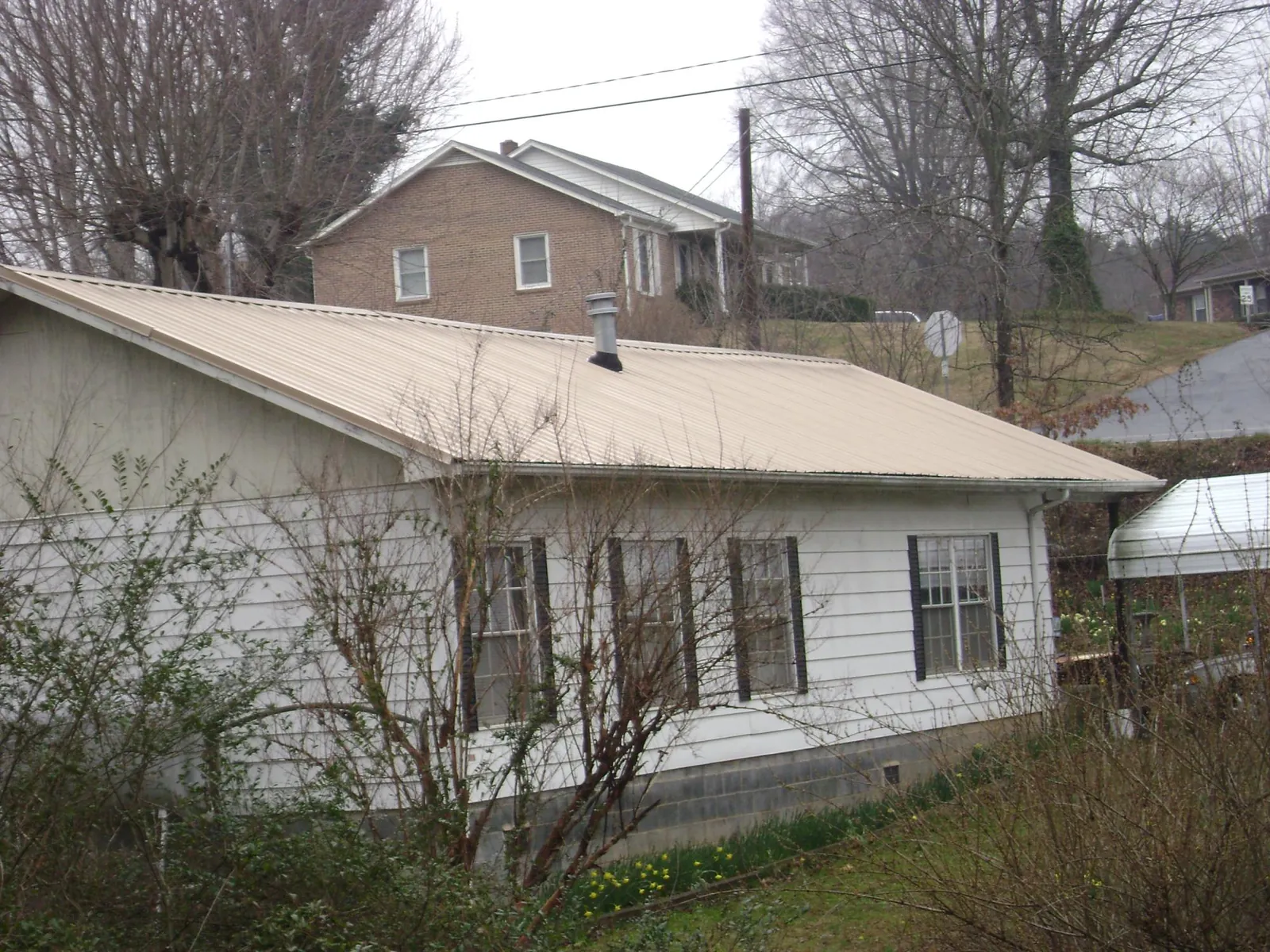 Tan metal roof on a white sided house set into a hillside — Commercial Roofing by Roofing Brothers in Noblesville