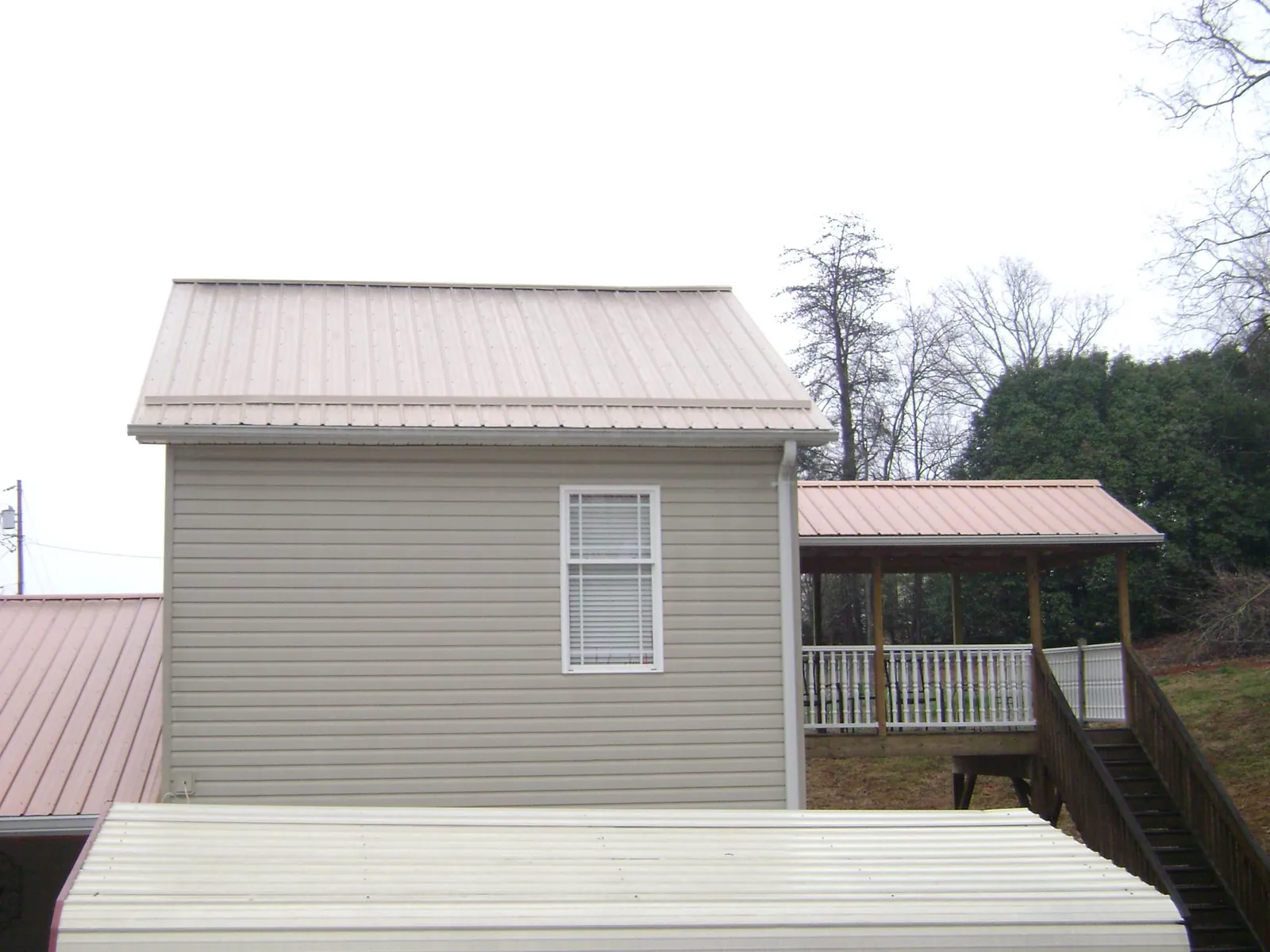 Tan metal roofs on a two story addition and attached porch, from a Roof Replacement job in Noblesville
